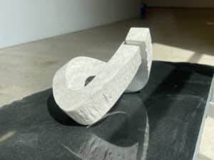 Skulptur namens "Klangskulptur. Die Weiße teilweise eliptische Skulptur aus kroatischem Kalkstein befindet sich auf einer schwarzen Platte